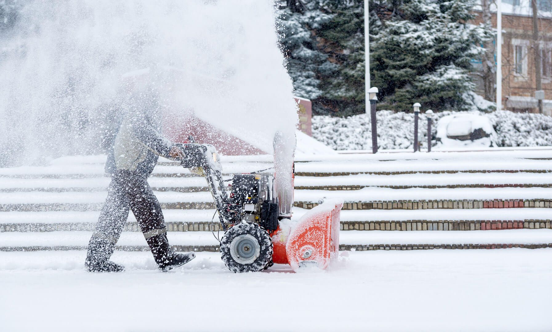 Eine Person bei Winterdienstarbeiten mit einer Schneefräse